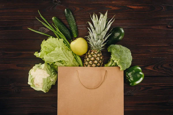 Vista superior de verduras y frutas verdes en bolsa de compras en mesa de madera - foto de stock