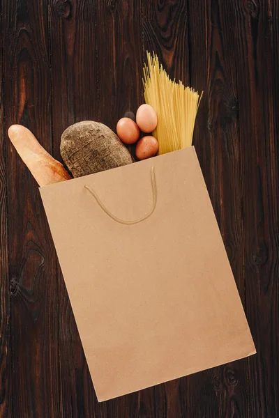 Vista superior del pan, pasta y huevos en la bolsa de la compra en la mesa de madera, concepto de supermercado - foto de stock