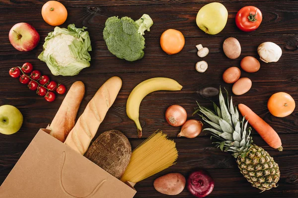 Вид зверху на овочі та фрукти з хлібом у сумці для покупок на дерев'яному столі, продуктова концепція — стокове фото
