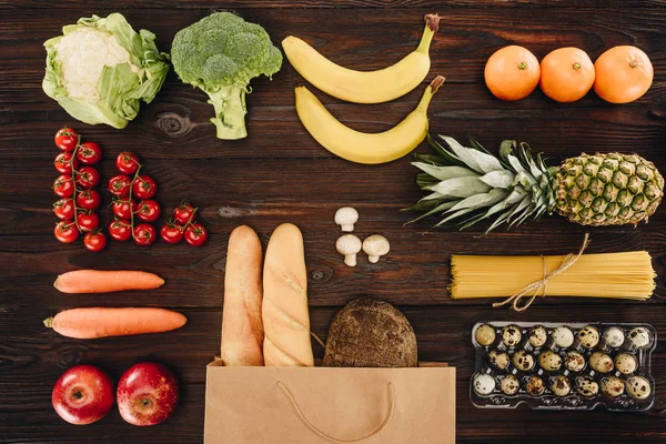 Вид зверху на овочі та фрукти з хлібом та макаронами на дерев'яному столі, продуктова концепція — стокове фото