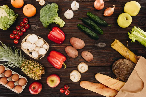 Вид зверху на овочі та фрукти з хлібом у сумці для покупок на дерев'яному столі — стокове фото