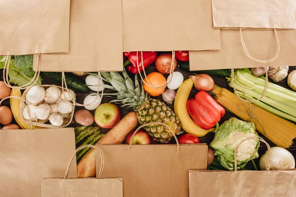 Vue du dessus des sacs à provisions couvrant légumes et fruits sur table en bois — Photo de stock