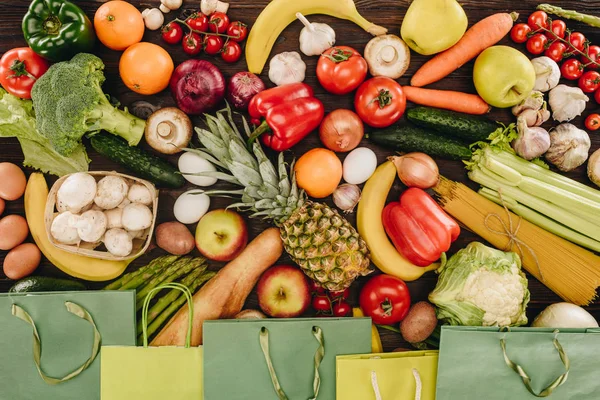 Верхний вид овощей и фруктов с бумажными пакетами на деревянном столе — стоковое фото