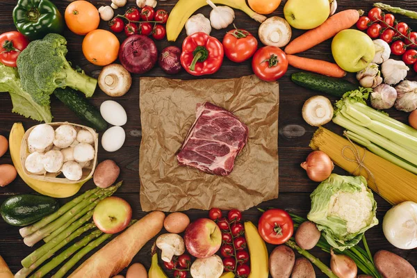 Blick von oben auf rohes Fleisch zwischen Gemüse und Obst auf Holztisch — Stockfoto