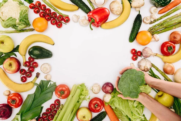 Immagine ritagliata di ragazza che tiene broccoli sopra la tavola con verdure e frutta isolate su bianco — Foto stock
