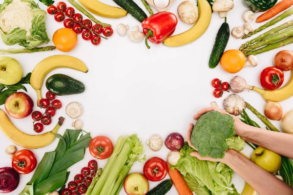 Abgeschnittenes Bild eines Mädchens mit Brokkoli über dem Tisch mit Gemüse und Früchten isoliert auf weißem Grund — Stockfoto