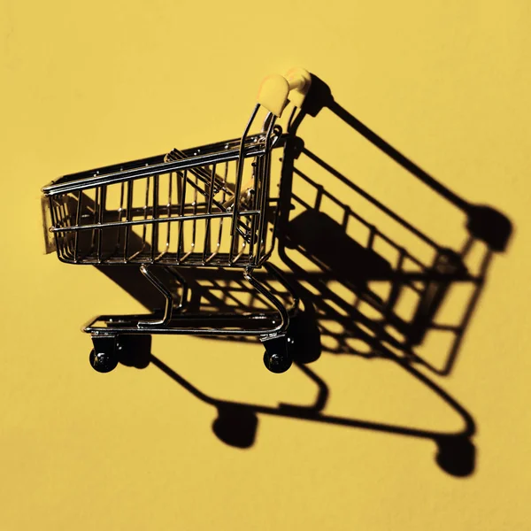 One shopping cart with shadow on yellow wall — Stock Photo