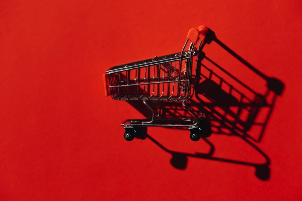 Um carrinho de compras com sombra na parede vermelha — Fotografia de Stock