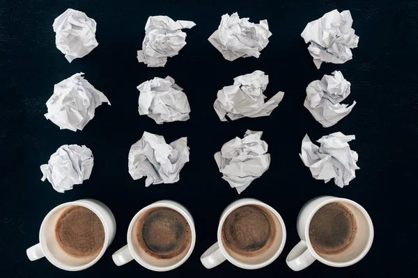 Top view of crumpled papers and cups of coffee in rows isolated on black — Stock Photo