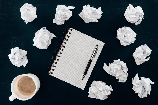 Top view of blank notepad with messy crumpled papers and cup of coffee isolated on black — Stock Photo