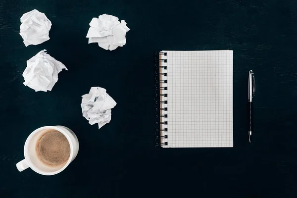 Top view of blank notebook with messy crumpled papers and cup of coffee isolated on black — Stock Photo