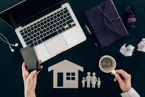 Recortado tiro de abogado de familia utilizando teléfono inteligente en el lugar de trabajo con la casa y la familia recortar figuras aisladas en negro - foto de stock