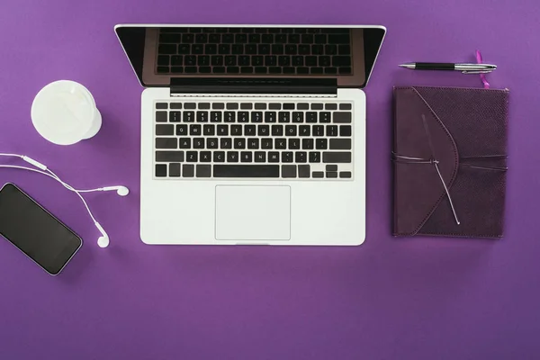 Top view of modern workplace with laptop on purple surface — Stock Photo