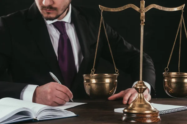 Cropped shot of lawyer doing paperwork at workplace with scales isolated on black — Stock Photo