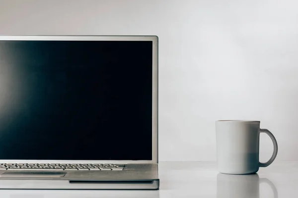 Laptop with cup of coffee on work table — Stock Photo