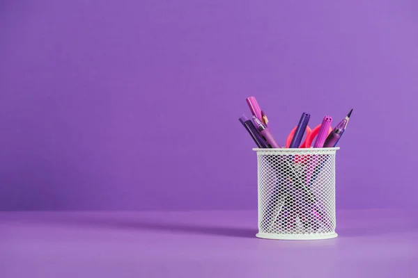 Porte-stylo avec divers stylos et crayons sur la surface violette — Photo de stock