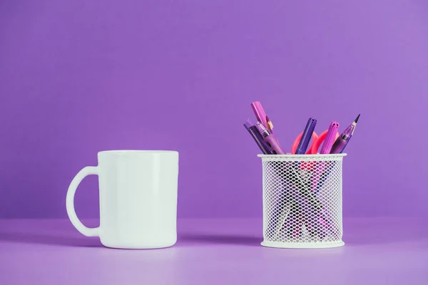 Taza y soporte de la pluma en la superficie púrpura - foto de stock