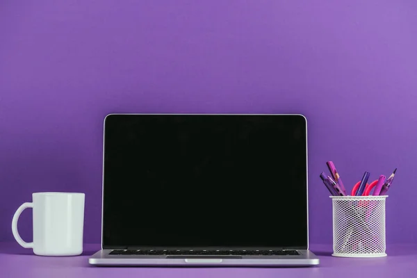 Рабочее место с ноутбуком и кружкой кофе на фиолетовой поверхности — стоковое фото