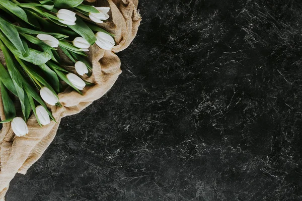Draufsicht auf weiße Tulpenblüten auf Tischdecke auf schwarzer Oberfläche — Stockfoto
