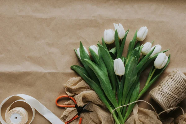 Top view of white tulips with ribbon and scissors on craft paper for international womens day — Stock Photo