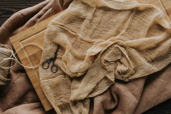 Vista superior de cordel e tesoura vintage na toalha de mesa e placa de madeira — Fotografia de Stock