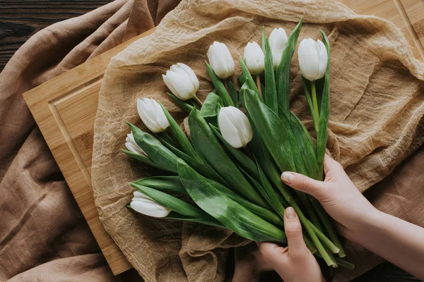 Cropped view of woman with bouquet of tulips on tablecloth and wooden board for 8 march — Stock Photo