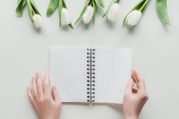 Vue recadrée de la femme avec cahier avec tulipes blanches sur la surface blanche — Photo de stock