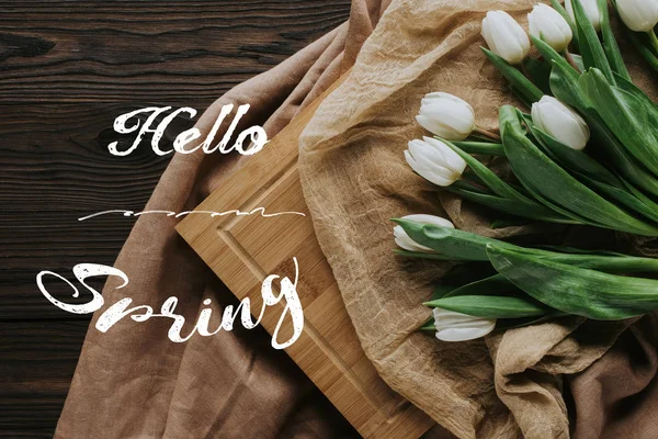 Vue de dessus des tulipes de printemps sur la nappe et la planche en bois avec lettrage de printemps bonjour — Photo de stock