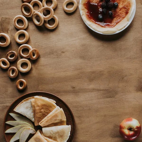 Top view of tasty homemade pancakes with jam and berries, apple and bagels on wooden table — Stock Photo