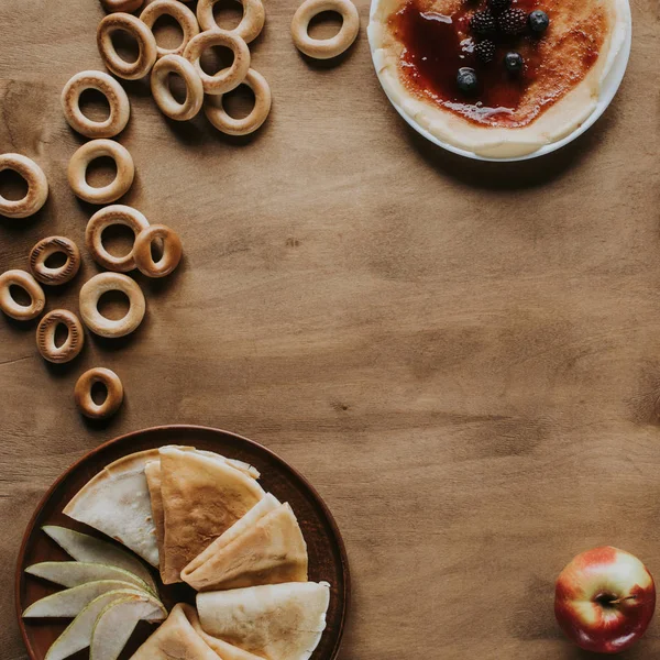 Vista superior de sabrosos panqueques caseros con mermelada y bayas, manzana y rosquillas en mesa de madera - foto de stock