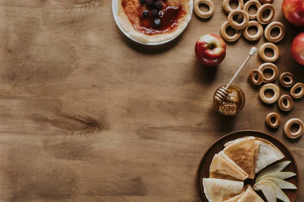 Blick von oben auf leckere Pfannkuchen mit Äpfeln, Beeren, Honig und Bagels auf Holztisch — Stockfoto