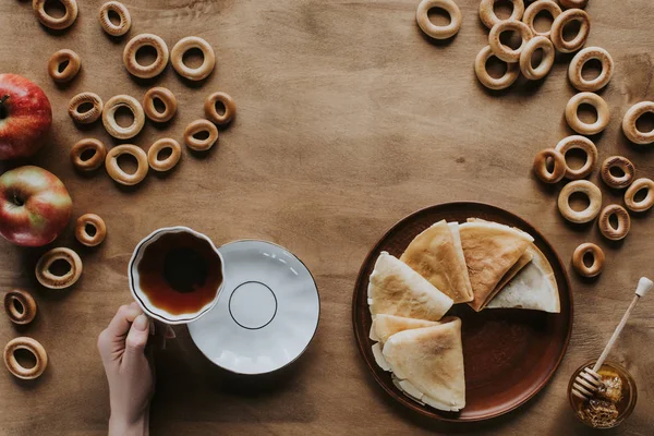 Plan recadré d'une personne buvant du thé et mangeant des crêpes à table en bois — Photo de stock