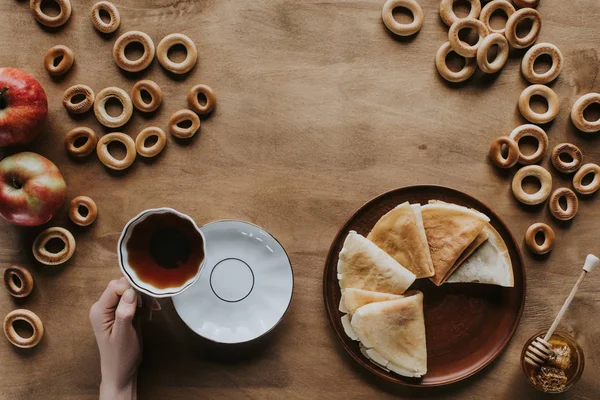 Cropped shot of person drinking tea and eating pancakes at wooden table — Stock Photo