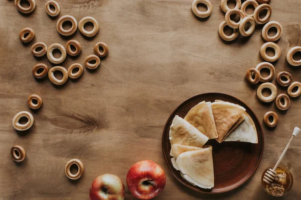 Вид зверху на млинці з яблуками, медом та бубликами на дерев'яному столі — стокове фото