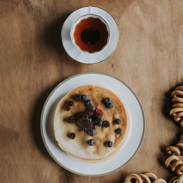 Blick von oben auf leckere Pfannkuchen mit Beeren, Tee und Bagels auf Holztisch — Stockfoto