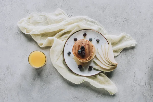 Blick von oben auf leckere hausgemachte Pfannkuchen mit frischen Früchten und einem Glas Saft auf grau — Stockfoto