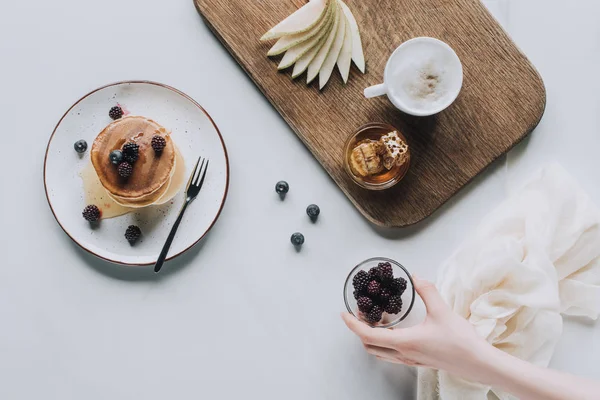 Обрезанный снимок человека с ежевикой и вкусный здоровый завтрак на сером — стоковое фото