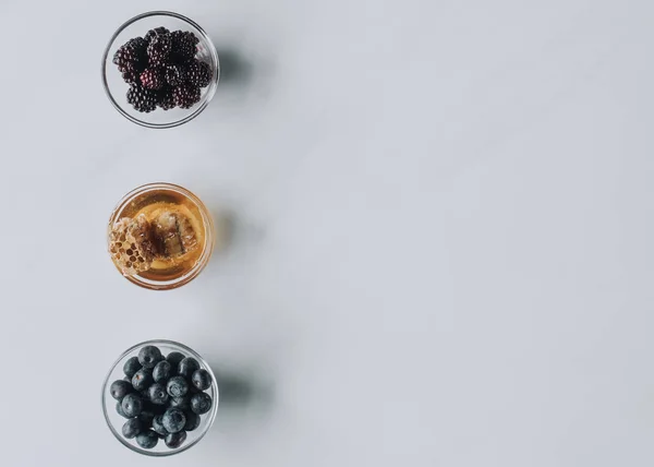 Вид сверху на стеклянные чаши с ягодами и медом, изолированные на сером — стоковое фото