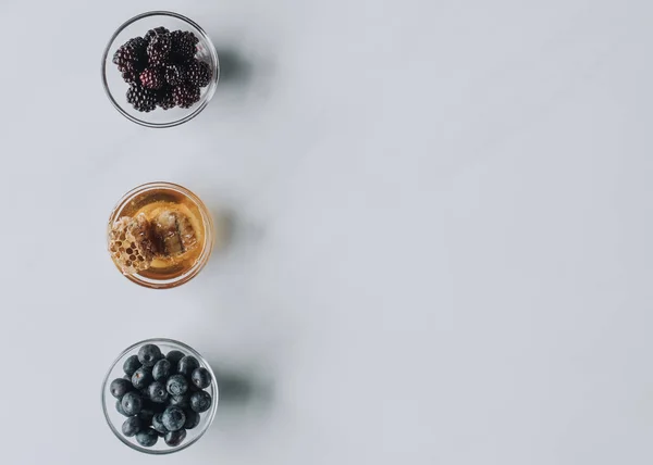 Vue de dessus des bols en verre avec des baies et du miel isolé sur gris — Photo de stock