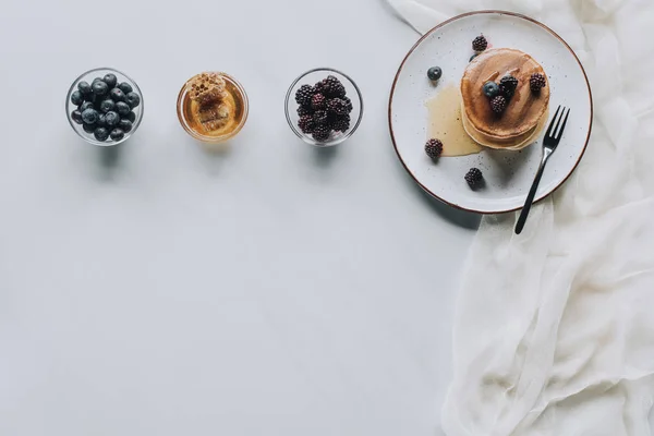 Top view of sweet homemade pancakes with honey and fresh berries on grey — Stock Photo