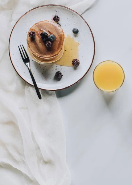 Vista superior de sabroso desayuno saludable con panqueques caseros, bayas, miel y jugo en gris - foto de stock