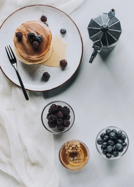 Top view of tasty breakfast with pancakes, berries, honey and coffee on grey — Stock Photo