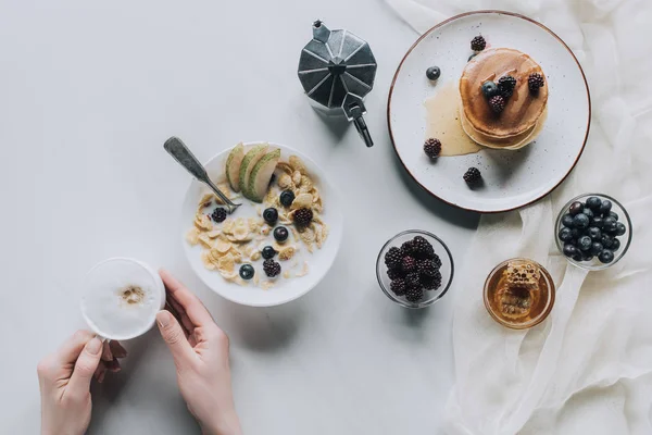 Colpo ritagliato di persona che tiene in mano una tazza di cappuccino mentre fa una gustosa colazione — Foto stock