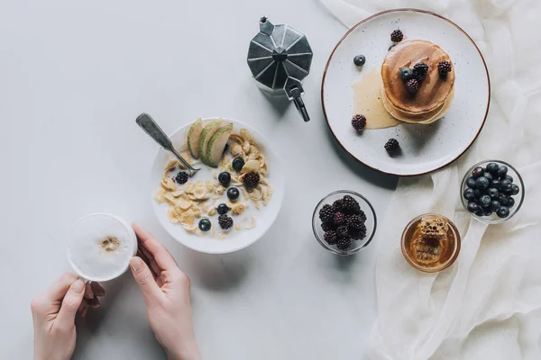 Tiro recortado de la persona sosteniendo taza de capuchino mientras desayuna sabroso - foto de stock