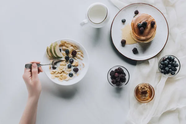 Tiro cortado da pessoa que come o café da manhã saudável fresco com muesli e panquecas — Fotografia de Stock