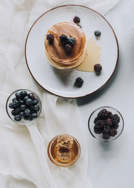 Vista superior de sabrosos panqueques caseros con miel, arándanos y moras en gris - foto de stock