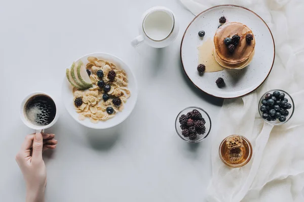 Vista superior de la persona sosteniendo la taza de café durante el desayuno saludable - foto de stock