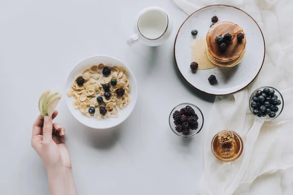 Tiro cortado de pessoa comendo muesli saudável e panquecas com frutas para o café da manhã em cinza — Fotografia de Stock