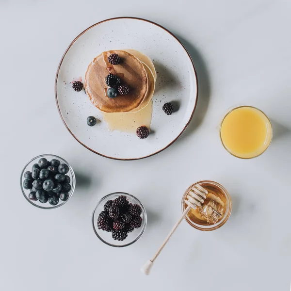 Blick von oben auf frische leckere Pfannkuchen mit Honig, Beeren und Saft auf grau — Stockfoto