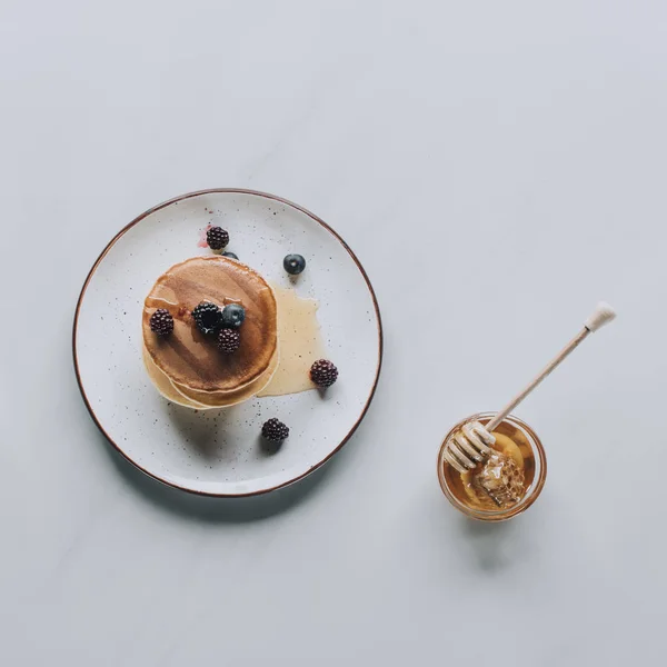 Süße hausgemachte Pfannkuchen mit Honig und Beeren auf grau — Stockfoto